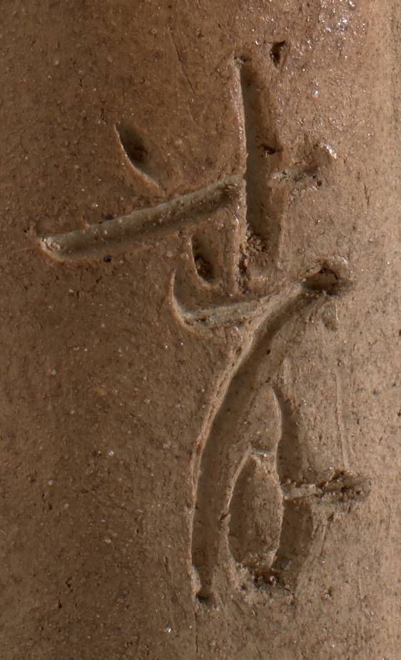 A gourd-shaped ceramic vase with vertical ridges and a loop of clay vine at the top. A dark hole near the center of the vase is surrounded by incised Japanese calligraphy.