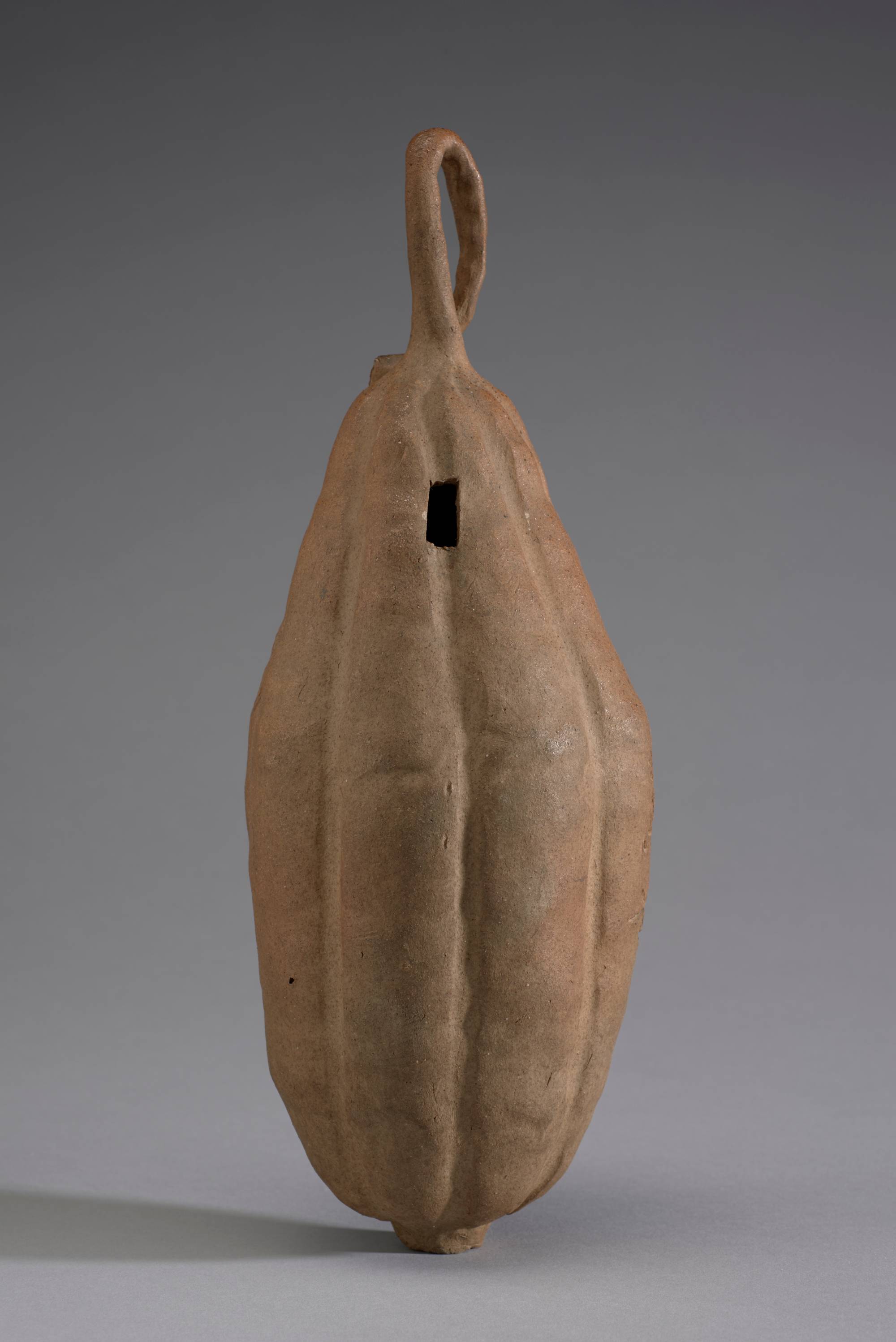 A gourd-shaped ceramic vase with vertical ridges and a loop of clay vine at the top. A dark hole near the center of the vase is surrounded by incised Japanese calligraphy.
