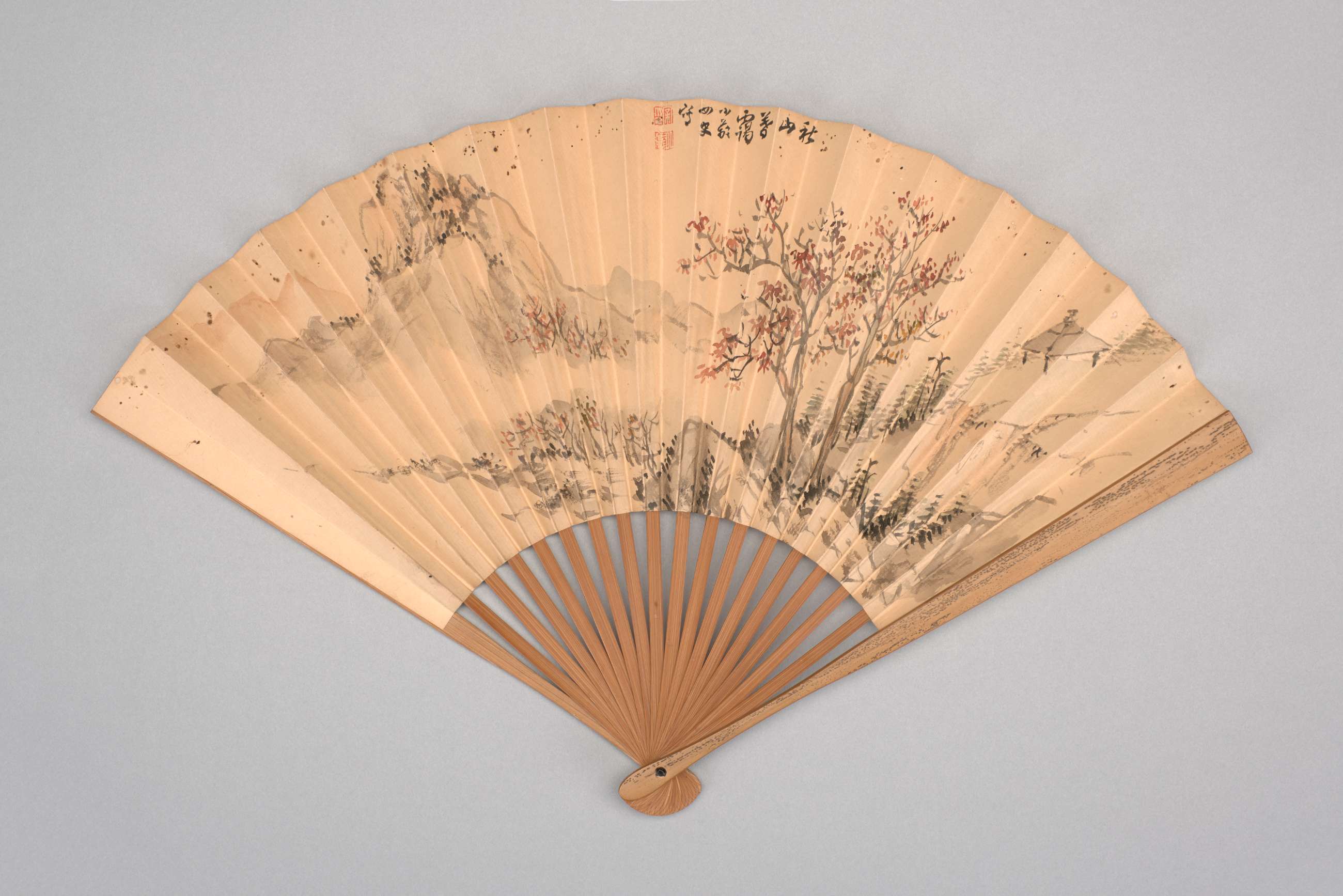 Cream colored paper folding fan painted with mountain scene with red leaf tree.