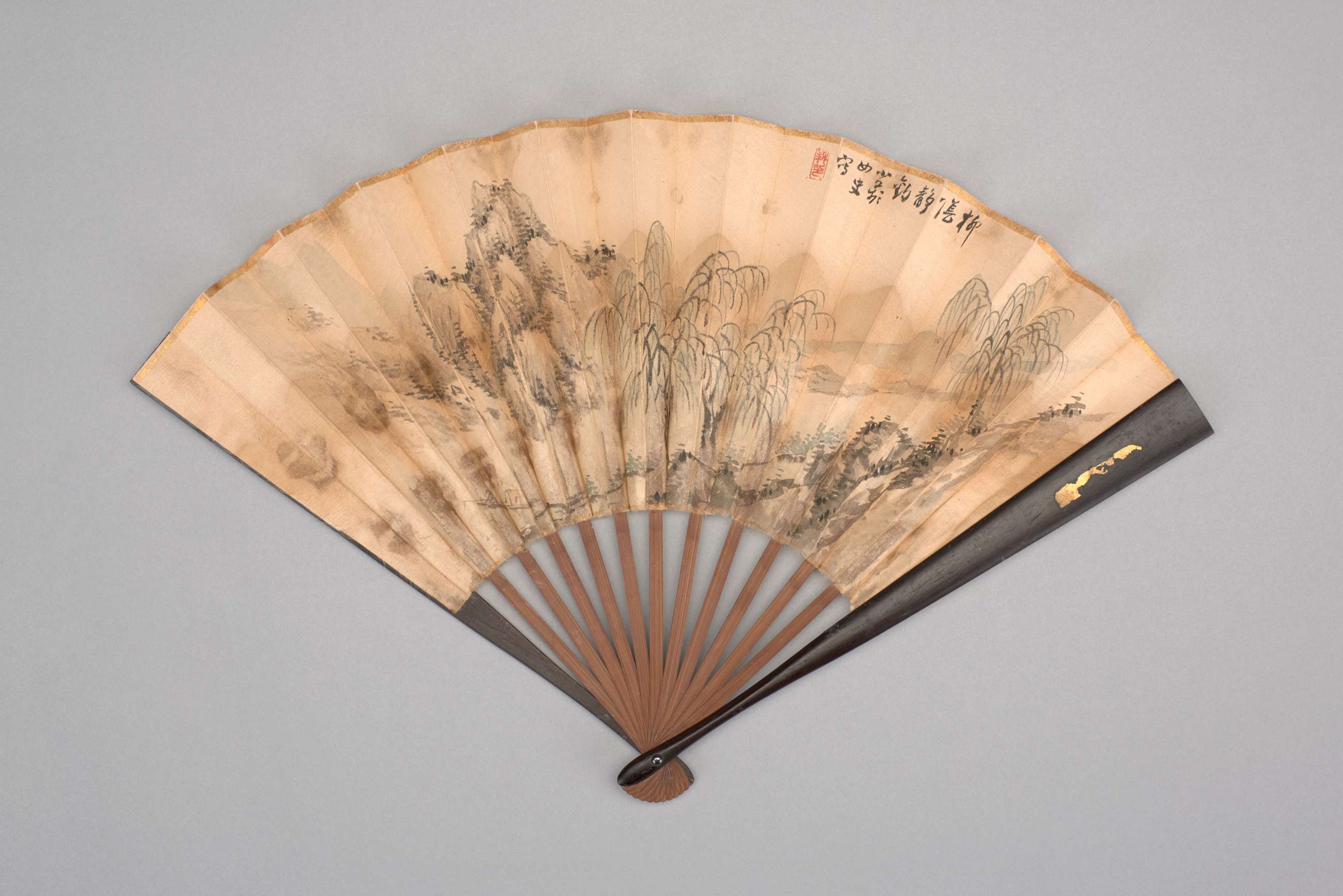 Cream colored paper folding fan painted with mountain scene.