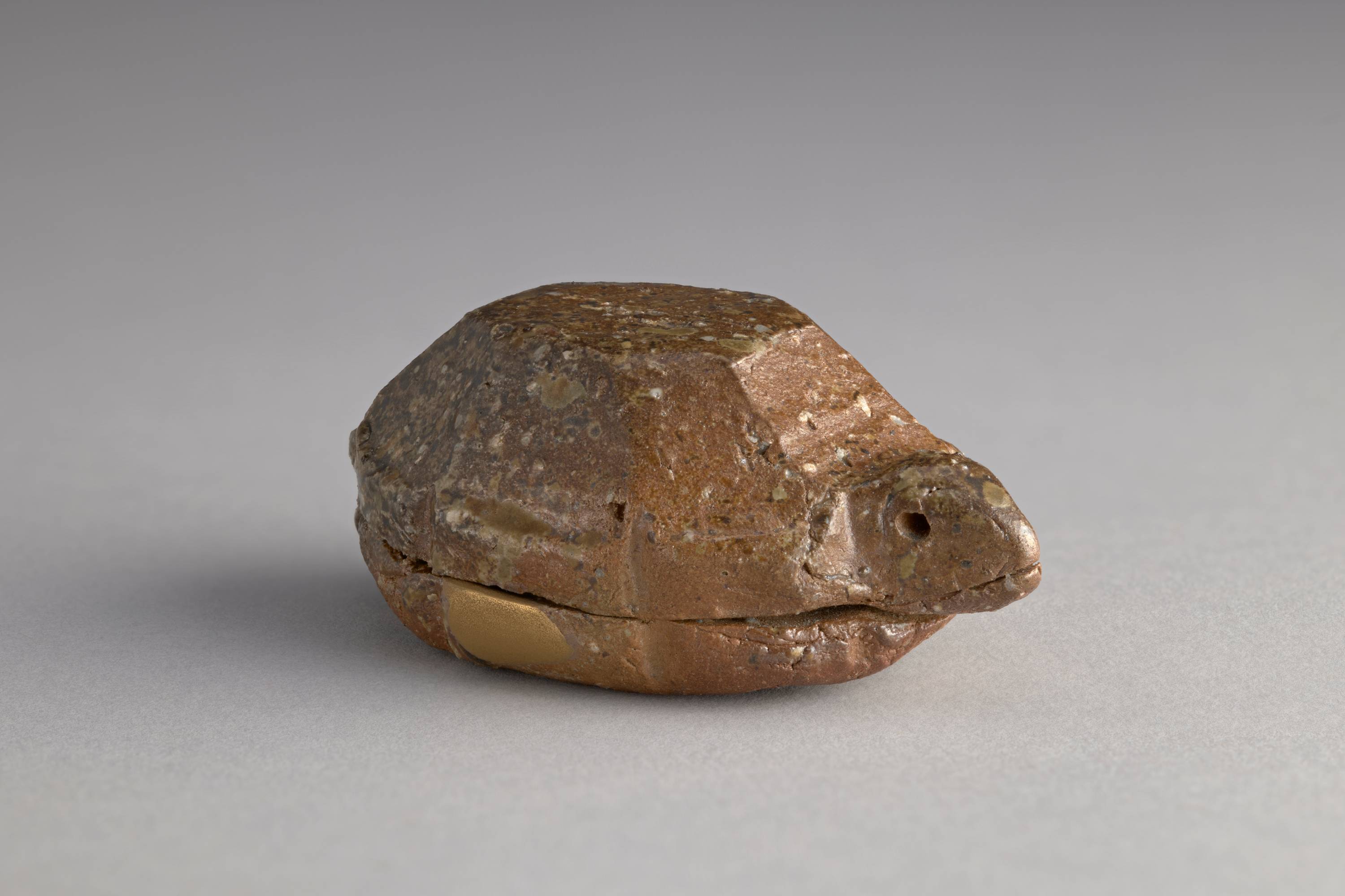 A small brown box in the shape of a tortoise. The lid is the head and shell of the tortoise. It has eight faceted sides, and the eyes of the tortoise are holes on either side of the head.