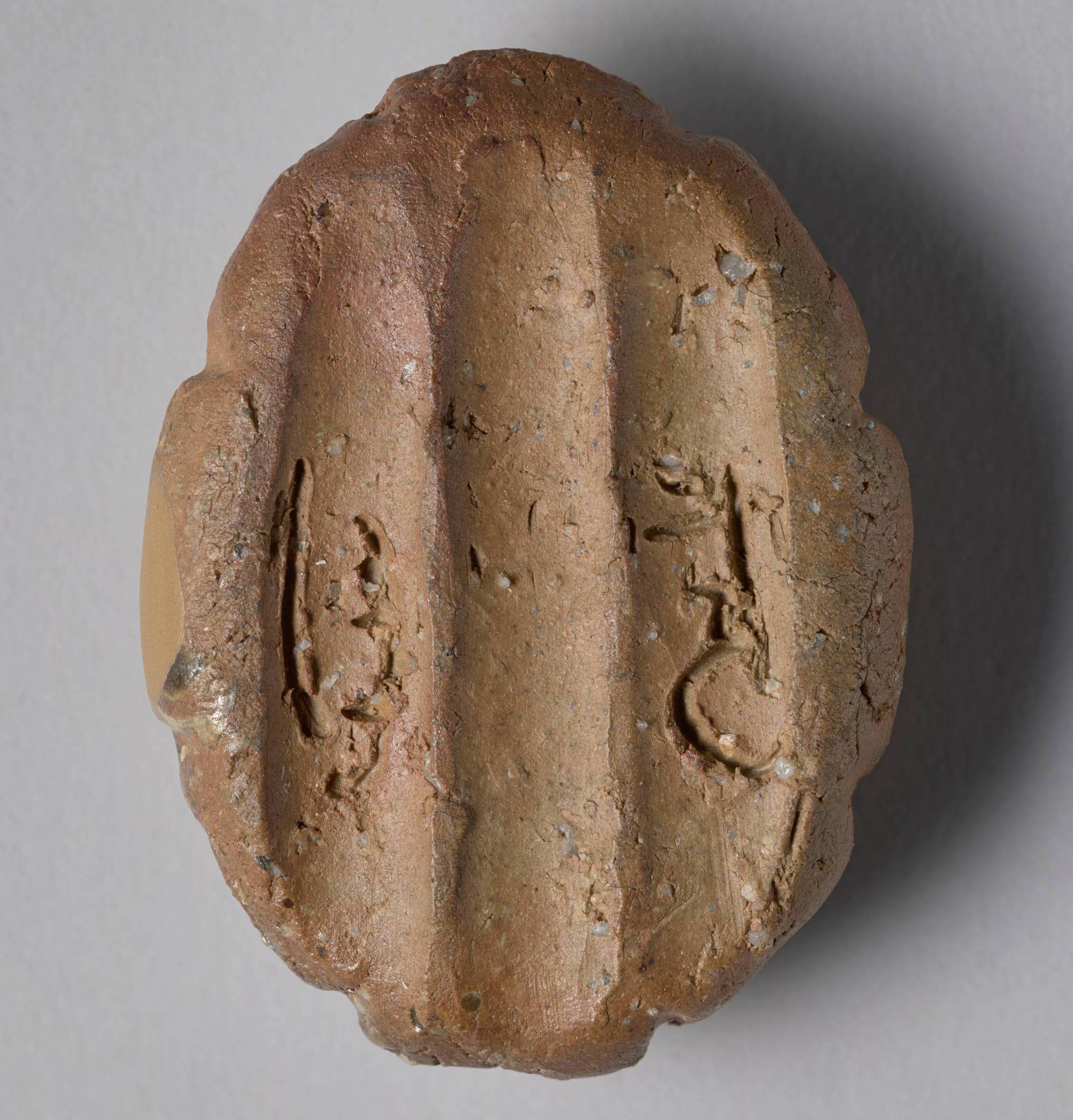 The bottom of a small brown box in the shape of a tortoise. It has eight faceted sides, and there are three finger-wide grooves that run from front to back. There is a rough-carved inscription of two characters, which represent the artist's name, Rengetsu.