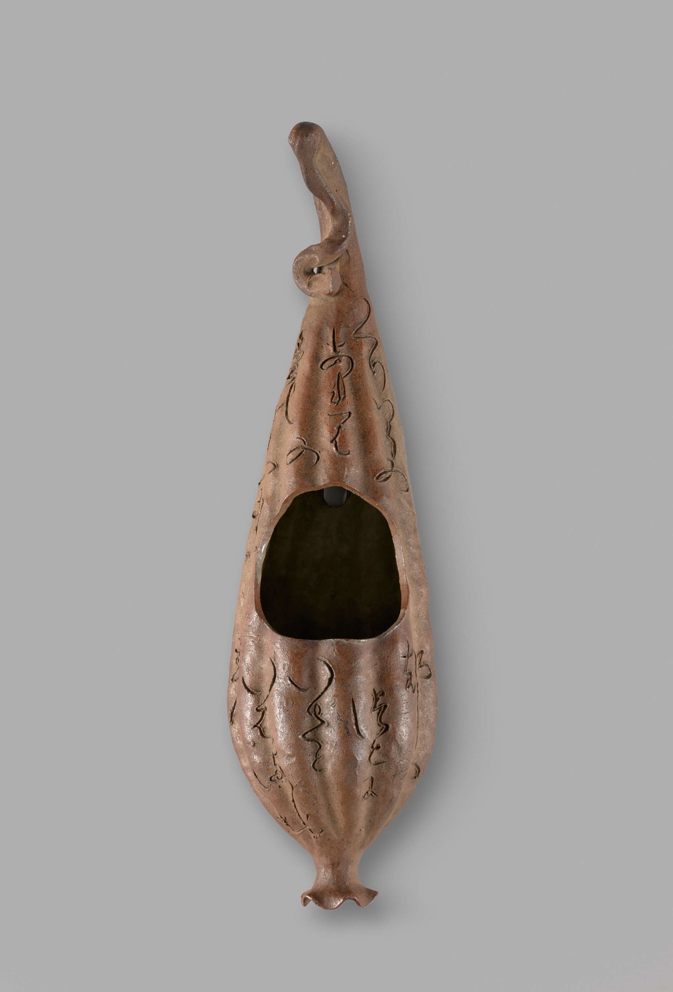 A gourd-shaped vase with vertical ridges. A dark hole in the center takes up about one third of the surface area.