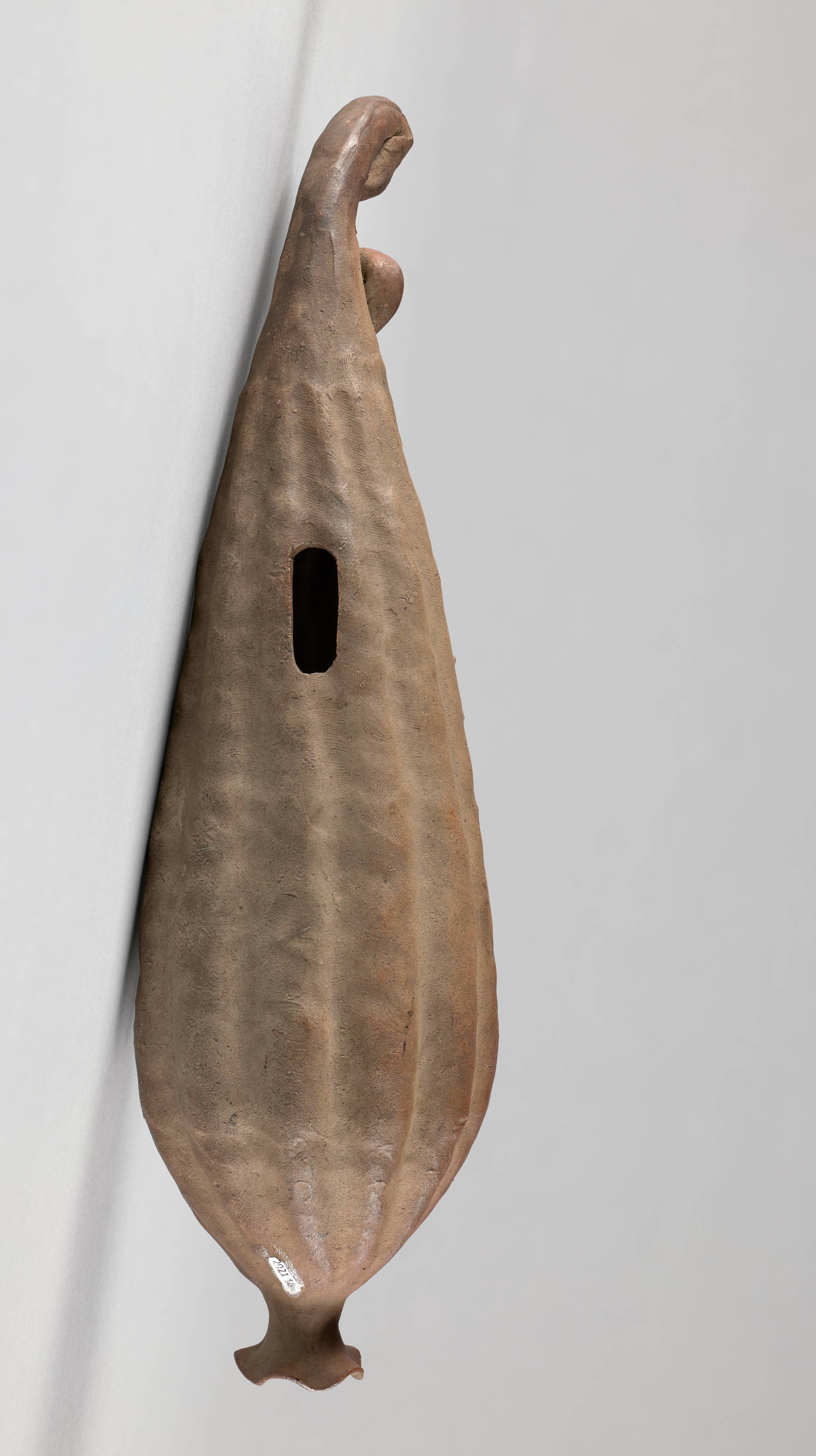 A gourd-shaped vase with vertical ridges. A dark hole in the center takes up about one third of the surface area.