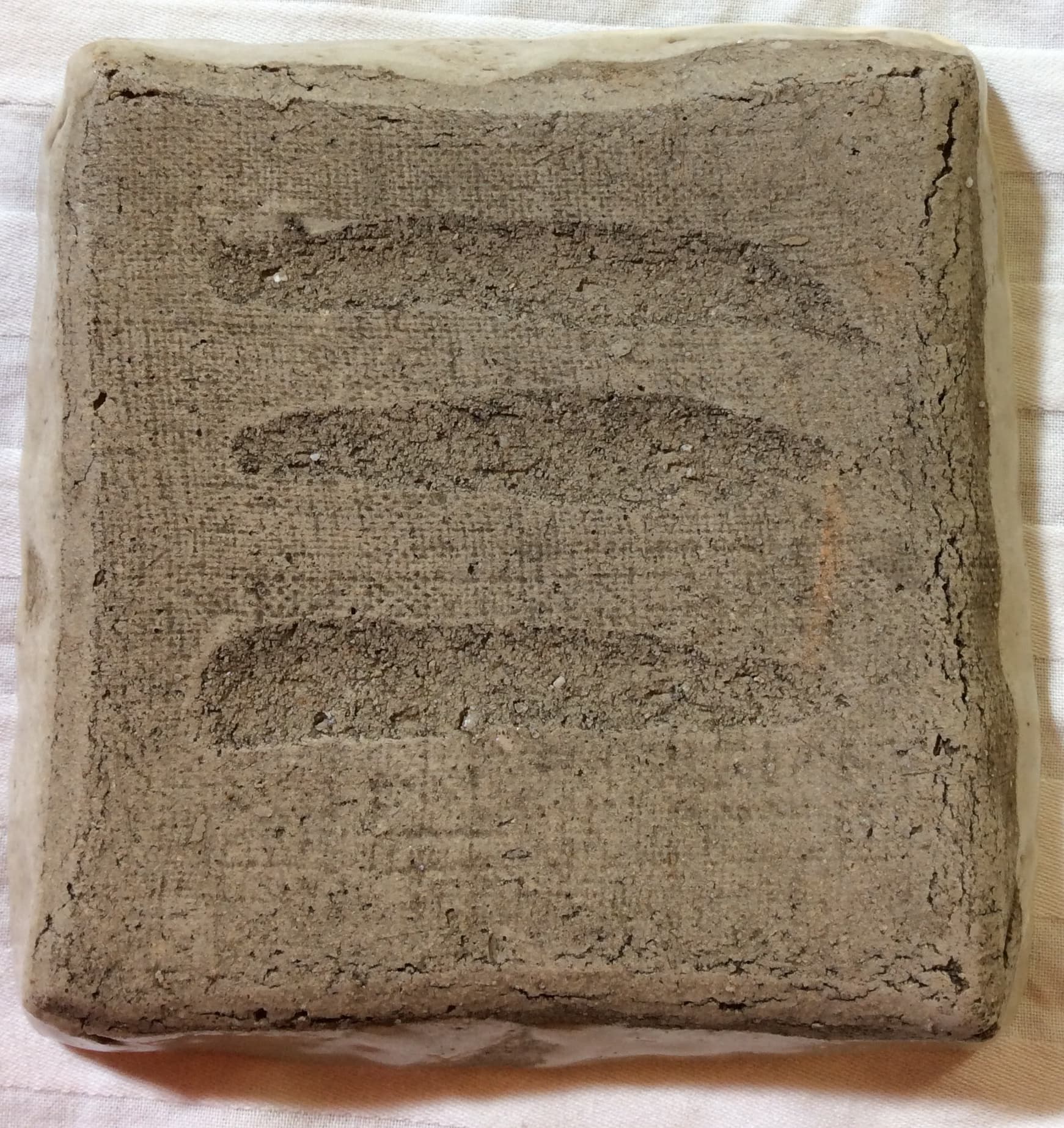 The bottom of a square plate with three horizontal marks made by fingers run through the wet clay.