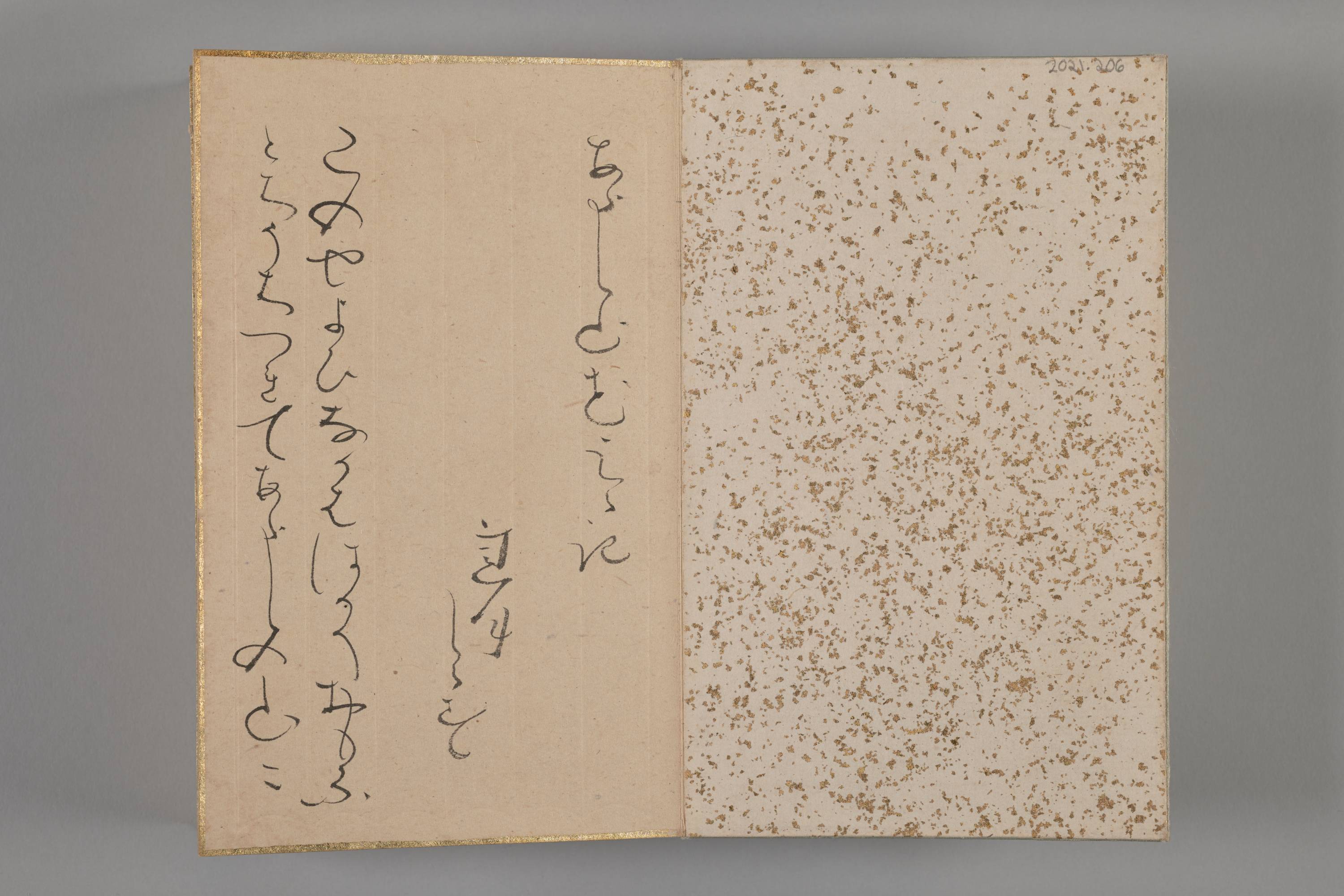 Two-page spread of a bound album with several vertical lines of cursive poetry on the left page. The inside back cover speckled with gold is on the right.