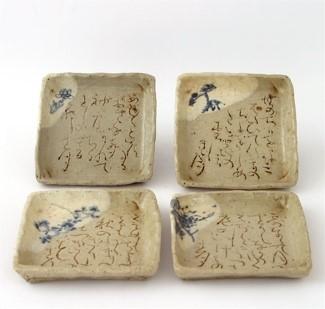 A set of four square ceramic plates with raised edges. The top left corner of each plate is lighter in color and features a floral motif. The rest of each plate is filled with Japanese calligraphy.