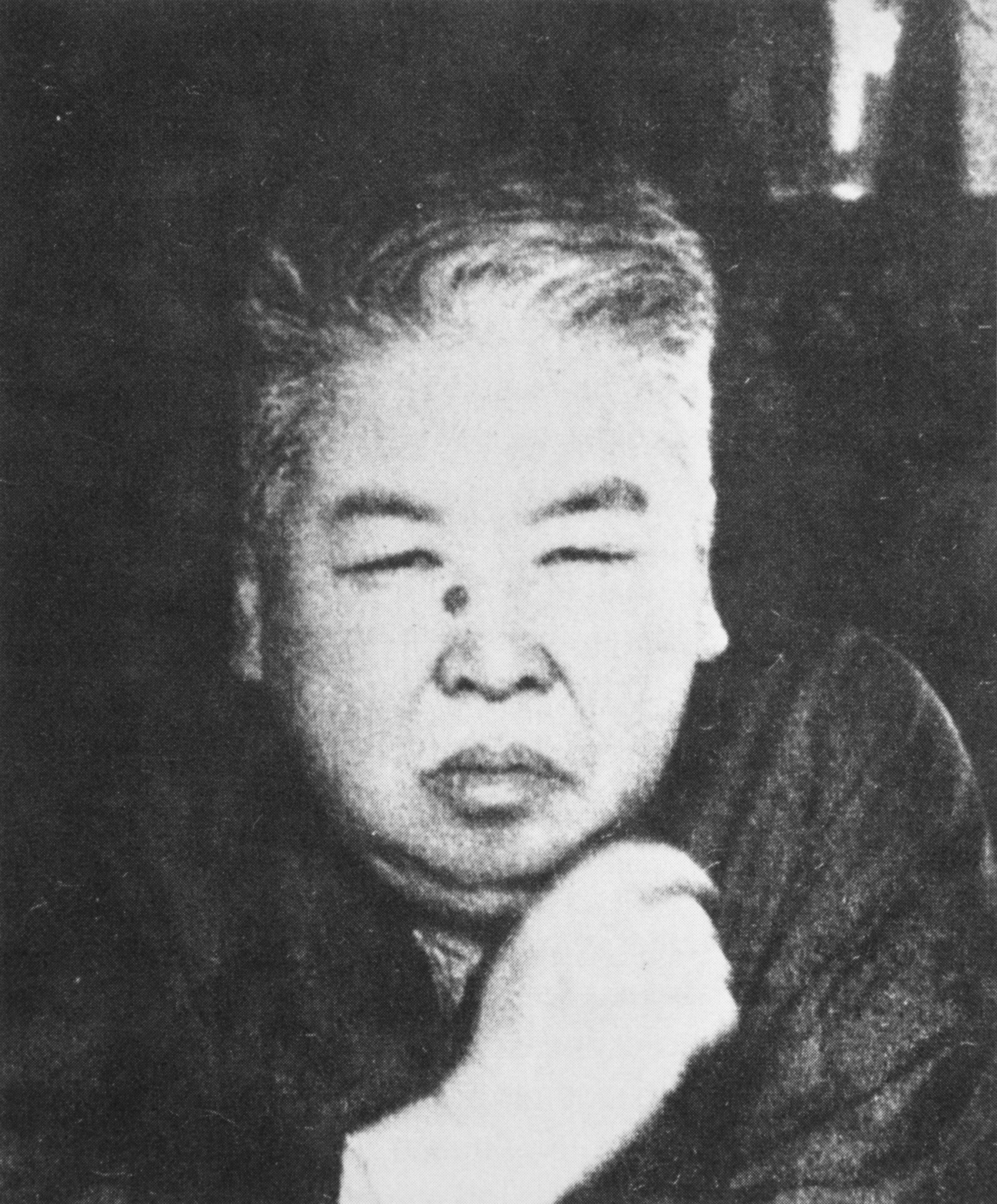 a black-and-white photo of a bust of a person with short cropped hair who stares out at the viewer with their right hand near their chin.